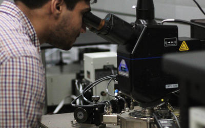 Samuel Márquez Gonzalez leans forward to look through a microscope in the lab. 