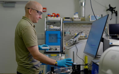 Thomas Forbes wears safety glasses as he looks at the screen attached to a piece of equipment in the lab. 