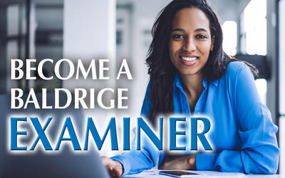 Woman sitting at a table while leaning on her hand and using her laptop to apply to become a Baldrige examiner.