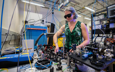 Alejandra Collopy wears safety glasses as she works the lab. She is surrounded by various pieces of equipment and many hanging wires. 