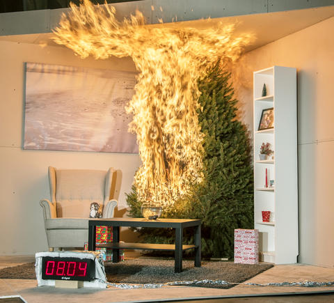 A Christmas tree is engulfed in flames. To the left is a chair. In front is a coffee table, rug and fishbowl. To the right is a tall bookshelf. There are 3 wrapped presents under the tree. A timer reads 8:04 seconds.
