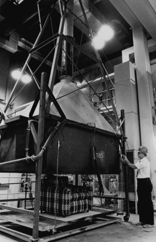 Fire Engineer Adjusting Furniture Calorimeter Black and white photo of a man standing in front of large piece of metal equipment shaped like a funnel. It reaches from the floor to the ceiling.