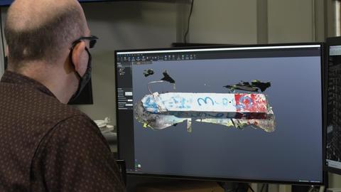 A researcher sits at a computer looking at a model of a broken piece of concrete on the screen. 