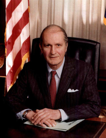 Secretary of Commerce Malcolm Baldrige sitting at desk.