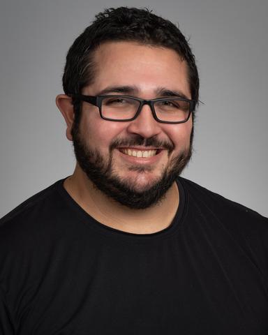 headshot of man with dark hair and beard wearing black shirt and glasses