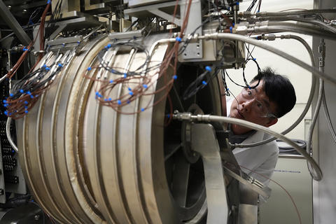 A researcher peers around the edge of large cylindrical piece of equipment in the lab. 