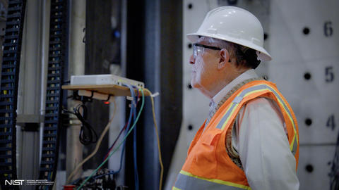A man in a hard hat and high-vis vest looks at something happening out of the frame. 