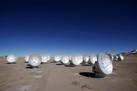 An array of large satellite dishes sits in the desert under a blue sky. 