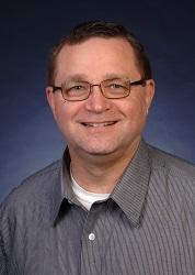 Michael R. Winchester, a person with short brown hair and glasses, smiling for the camera.