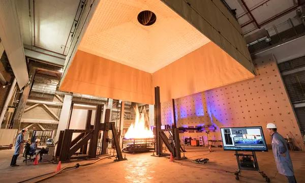 Photograph of large open room with fire engineers standing around a large fire test.