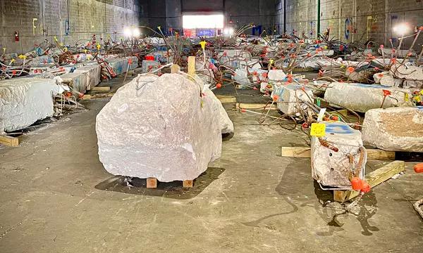 Large chunks of concrete bristling with rebar and colored flags sit in a warehouse. 