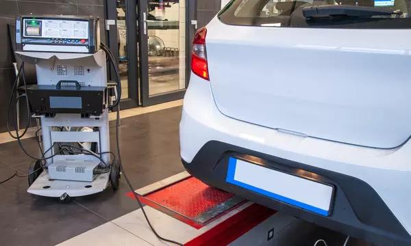 Photograph of an automobile at an emissions testing station, with testing equipment and probe positioned at the car tailpipe.