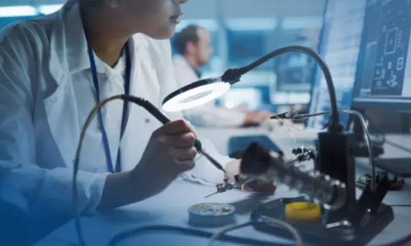 Person soldering and referencing a computer screen in a lab 