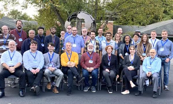 A group of workshop participants posing for a group photo with a globe statue and trees in the background.