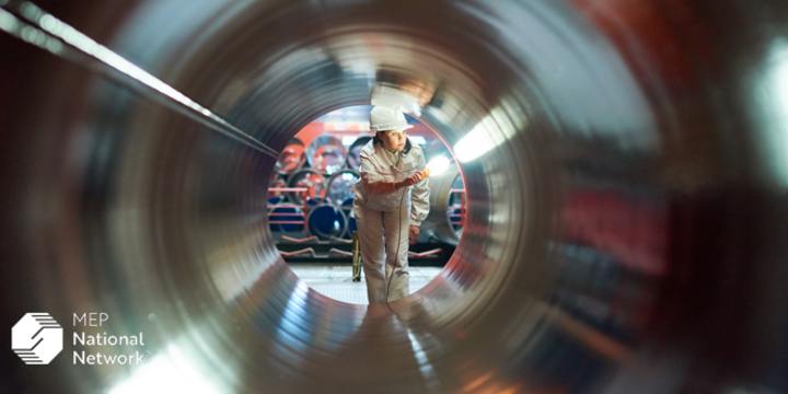 person quality inspecting a large metal pipe