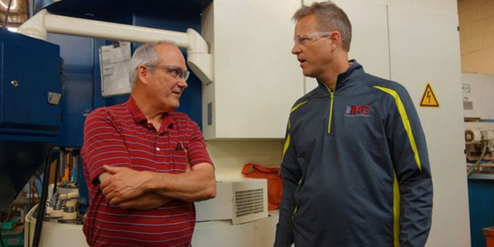 two men standing in a manufacturing factory talking about cobots