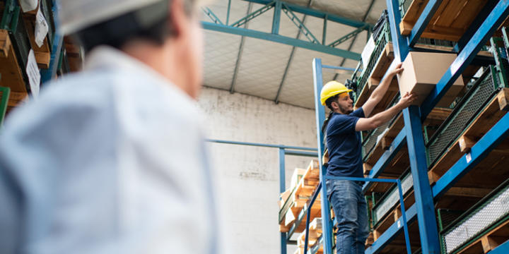 Warehouse worker on ladder searching for box with foreman assisting