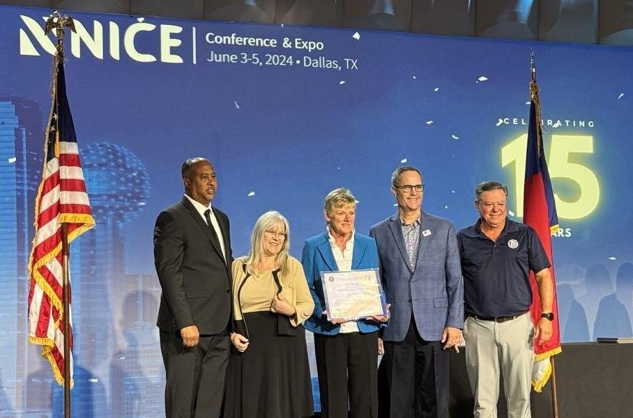 People on stage at the NICE conference standing between an American flag and Texas flag