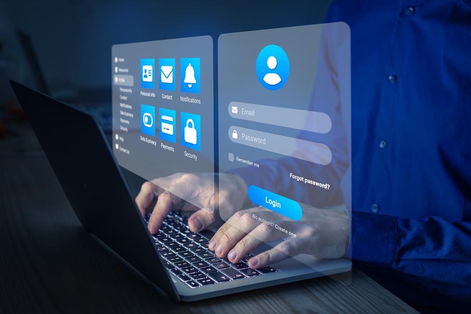 A person's hands hover over the keyboard of a laptop while an image floats above showing a login screen with email and password fields.
