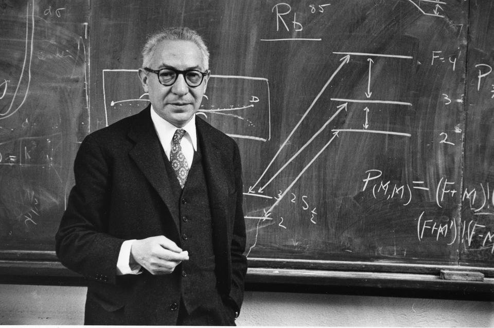 B&W photo shows Rabe standing in a suit in front of a chalkboard with physics formulas.
