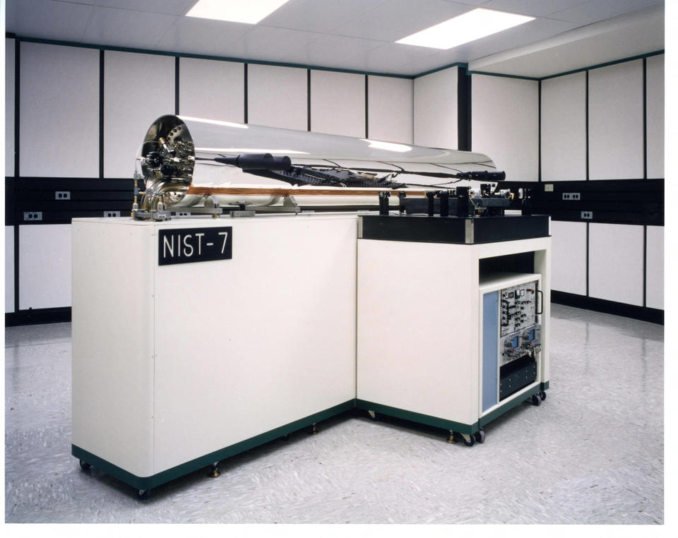 A large shiny silver-colored cylinder is mounted on white cabinetry with a sign saying "NIST-7."