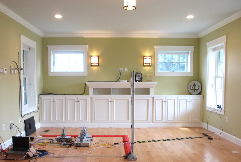 A living room is empty except for built-in cabinetry and scientific equipment, including four small heaters on the floor with associated wiring. 