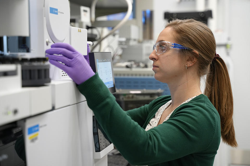 Briana Capistran wears safety glasses and purple gloves as she operates laboratory equipment. 