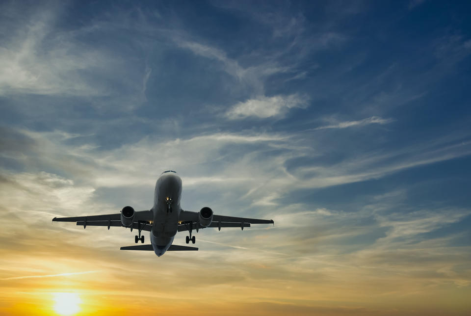 A passenger airplane seen from below takes off in front of a setting sun. 