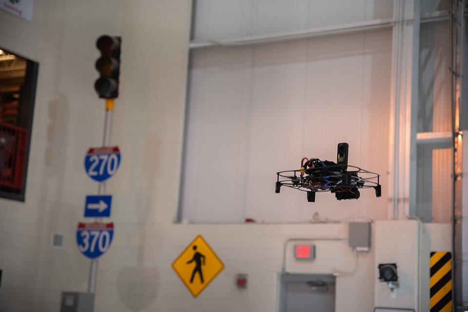 UAS in air inside a testing facility that includes street signs and stoplights. 
