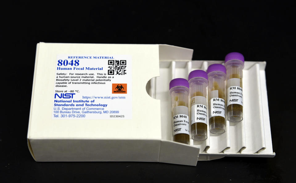 A white box labeled "8048 Human Fecal Material" lies open, with a tray of four plastic vials pulled out. 
