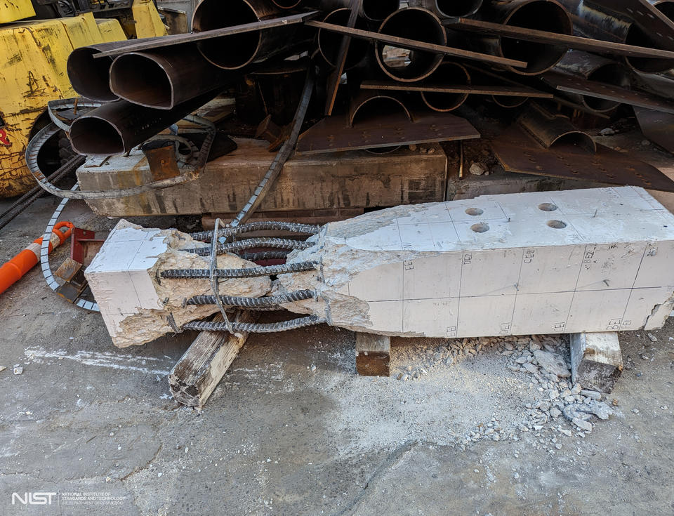 A broken concrete column lies on its side with a cracked portion where the rebar is exposed.