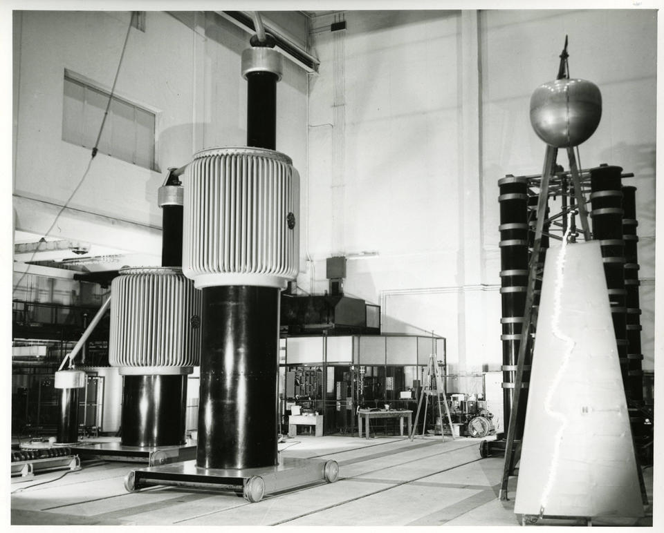 Historical photo shows a large lab space with cylindrical metal towers of different shapes. 