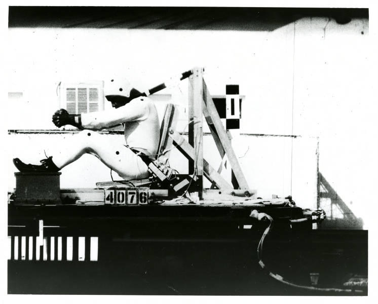 Historical photo shows test subject in helmet and bodysuit strapped into moving seat.