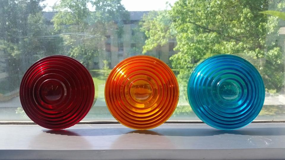 Three round colored lenses are displayed on a window ledge: red, orange and blue. 