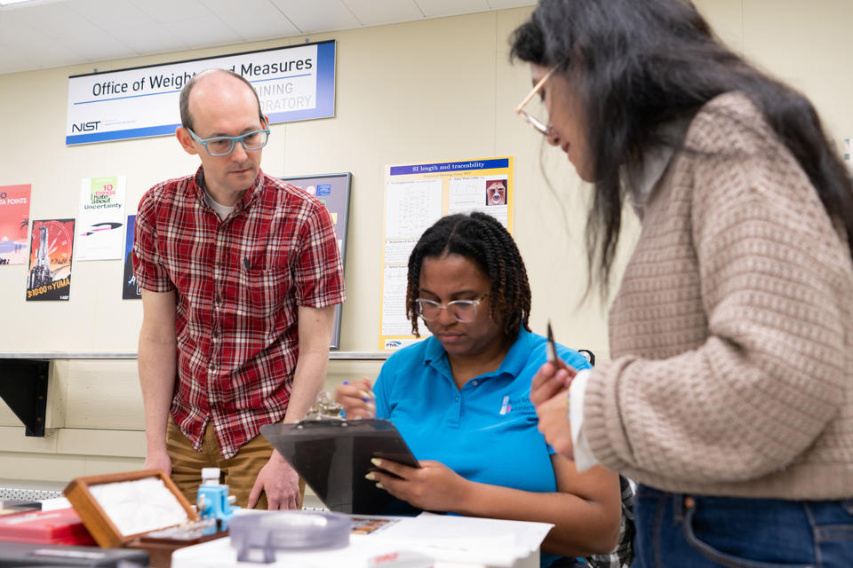 Tobias Herman, Instructor, collaborates with students attending a “Fundamentals of Metrology” course as they perform measurements in the Office of Weights and Measures Training Laboratory, Gaithersburg, Maryland.