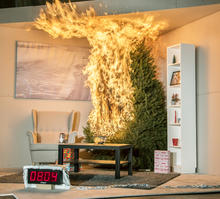A Christmas tree is engulfed in flames. To the left is a chair. In front is a coffee table, rug and fishbowl. To the right is a tall bookshelf. There are 3 wrapped presents under the tree. A timer reads 8:04 seconds.
