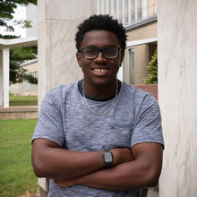 Miles Walker poses smiling, with his arms crossed, outside a building on the NIST campus. 