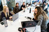 This image shows people sitting around a white table with laptops. In the foreground is two women with laptops.