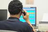 man holding land mobile radio up to ear while looking at a computer screen