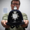 A blurry figure in the background holds out a black police helmet with a silver seal that reads "Norfolk Constabulary."
