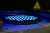 Photograph depicting IC manufacturing showing glowing squares on a round wafer, with a yellow triangular warning indicator labeled UV.
