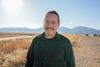 Zach Grey poses outdoors with wind turbines in the background. 