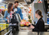 People checking out in a grocery store with person seated scanning items