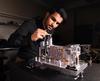 A person in a black shirt works on a mechanical device in a lab setting.