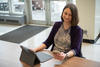 Julie Haney sits at a table in the NIST library with a laptop, looking at a smartphone in her hand. 