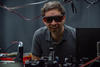 Krister Shalm, wearing safety glasses, smiles over a lab table covered with electronics equipment.