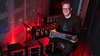 Scott Davis poses smiling and holding a frequency comb console. Other similar electronic products are stacked on carts around him. 